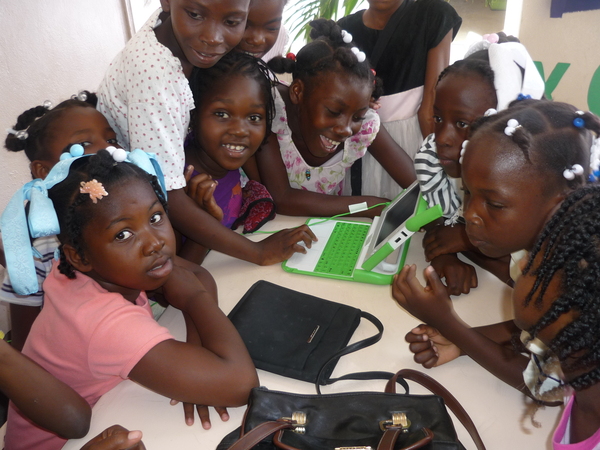 Group of girls from Haiti huddle around a single laptop for a class