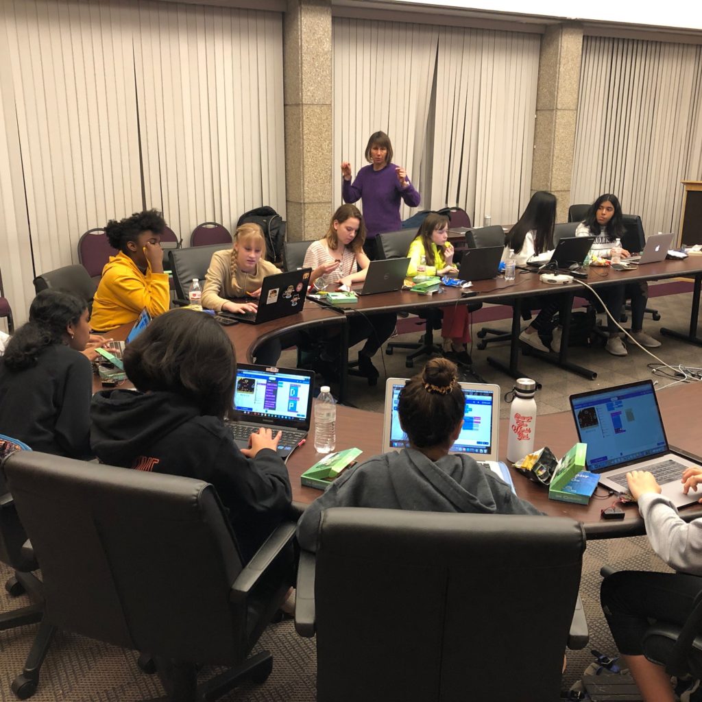 Girls sit around a rounded table and work on their laptops during a workshop