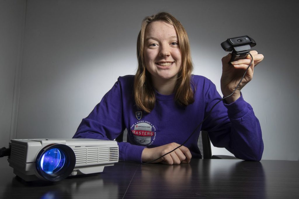 Teen girl holding a web cam attached to a projector.